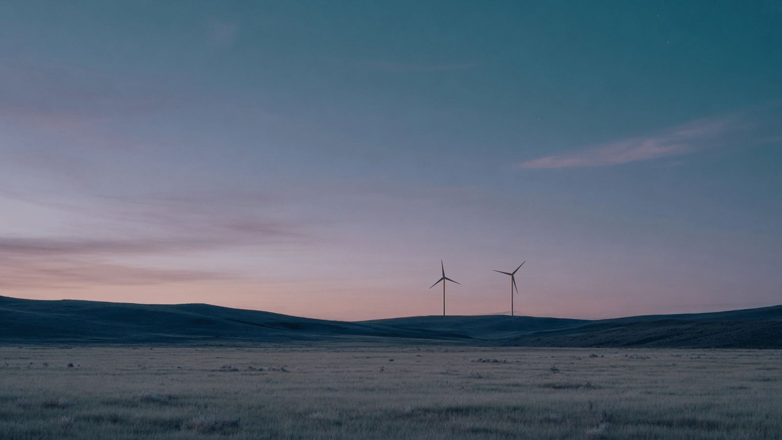 Two distant wind turbines turning on a quiet dusk hillside